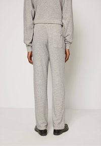 Siv svetar in usklajene trenirke z zadnjim žepom, sproščen kroj in mehak material, s črnimi čevlji, ki dopolnjujejo videz.