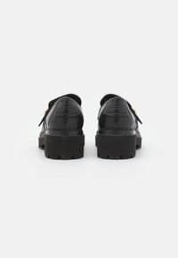 Zapatos de cuero negro con suela de goma gruesa, con un diseño redondeado y herrajes decorativos. Textura suave con detalles de costura.
