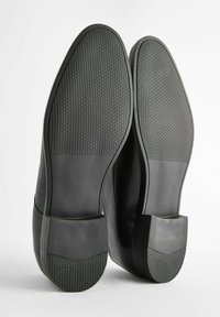 Zapatos de cuero negro con un diseño suave y suelas de goma texturizadas, que presentan acentos en el tacón angulares y un perfil elegante.