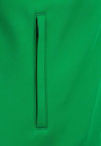 Tessuto per abbigliamento verde con una texture liscia, dotato di una tasca verticale con zip. I punti di cucitura corrispondono al colore del tessuto.