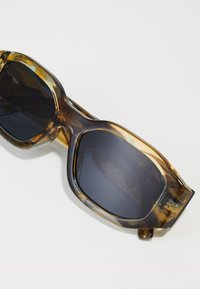 Gafas de sol de gran tamaño con un patrón de carey, acabado brillante, lentes oscuros y montura cuadrada gruesa. Presenta brazos de patilla anchos.
