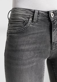 Jeans de denim gris ajustados que cuentan con una textura suave, un ligero efecto desgastado, cinco bolsillos y un cierre de botón metálico.