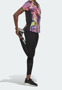 Sportovní outfit s topem s vícemořádným květinovým potiskem a černými legínami se síťovanými panely. Černé sportovní boty s bílými akcenty.