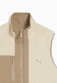Beige Fleece-Weste mit einem weichen, strukturierten oberen Abschnitt, einem kontrastierenden glatten Stoff darunter, einem Reißverschluss vorne und einem Logo-Akzent.