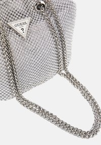 Hopeakankainen käsilaukku, jonka teksturoitu pinta on peitetty pienillä rhinestoneilla. Varustettu kolmiomaisella logolla ja metallisella ketjuhihnalla.