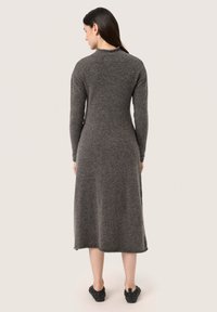 Abito grigio lavorato a maglia con maniche lunghe, design fit-and-flare e dettagli delle cuciture. Texture morbida e lunghezza fin sopra il ginocchio, abbinato a calzature nere.