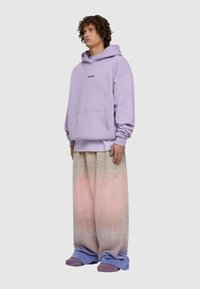 Lāveņu kapucēs džemperis ar priekšējo kabatu, kombinēts ar pārāk lieliem gradienta sporta biksēm rozā, zilā un zaļā kr āsā. Ietver purpursarkanas slīdēšanas apavus.