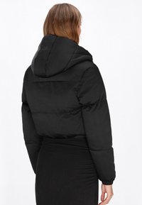 Giacca a vento corta nera con cappuccio. Presenta una texture trapuntata e polsini elasticizzati. Design semplice senza loghi o decorazioni visibili.