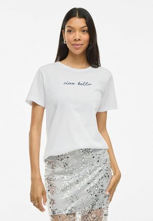 Witte katoenen t-shirt met korte mouwen en ronde hals, met de tekst "ciao bella" in marineblauwe cursieve letters. Draagt met een zilveren paillettenrok.