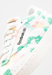 Sneaker Reebok con una toma superiore in spugna bianca, caratterizzate da motivi floreali verdi e rosa, lacci bianchi e suola in gomma testurizzata.