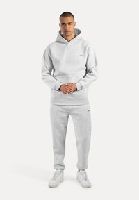 Jasnoszara bluza z kapturem, posiadająca przednią kieszeń oraz sznurek do regulacji kaptura, zestawiona z pasującymi spodniami dresowymi. Żywowana z białymi sneakerami.