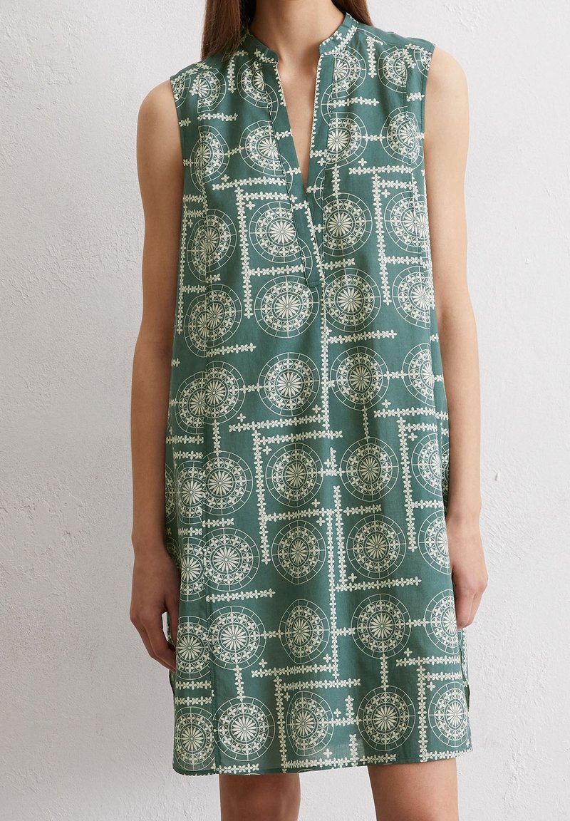 Ärmellös, knälång klänning i grönt med ett geometriskt vitt mönster. Har en kraglös halsringning och en avslappnad passform. Mjukt tyg.