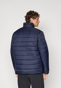 Chaqueta de plumas azul marino con costuras horizontales, cuello alto y textura suave. El diseño incluye un corte relajado y detalles de hardware mínimos.