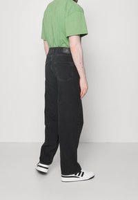 Černé džíny s uvolněným střihem, se dvěma zadními kapsami a jednoduchým pasem. V kombinaci se zeleným tričkem a bílými teniskami.