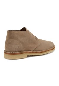 Stivaletti in suede beige con punta rotonda, due occhielli per i lacci, suola chiara a contrasto e dettaglio di cucitura attorno alla base.