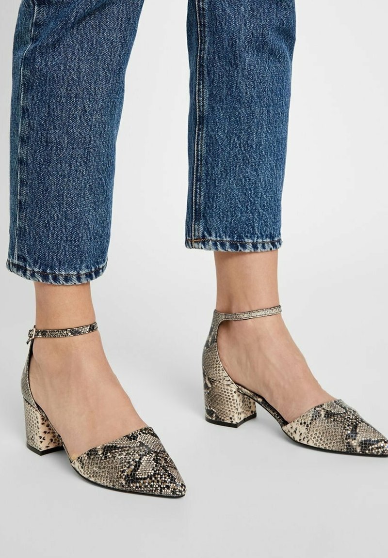 Chaussures à talons pointues avec un motif imprimé serpent, dotées d'une bride métallique autour de la cheville, avec un talon épais et une surface texturée.