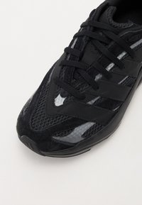 Baskets de sport noires avec tige en maille, accents en daim et superpositions en synthétique. Équipées de lacets ronds et d'une semelle texturée.