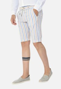 Pantaloni corti a righe in tessuto beige, blu e bianco con vita elastica regolabile, tasche laterali e taglio al ginocchio. Abbinati a scarpe slip-on grigie.