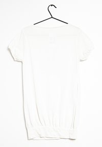 Top blanco de manga corta con cuello redondo, dobladillo fruncido y puños elásticos, colgado en un gancho negro sobre un fondo liso.