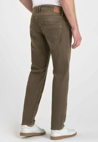 Jean slim fit en coton vert olive avec cinq poches, coutures visibles et une étiquette en cuir sur la taille arrière.