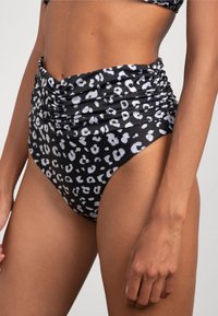 Costume da bagno a vita alta di colore nero con stampa leopardata bianca. Presenta dettagli arricciati sui lati per un aspetto testurizzato.