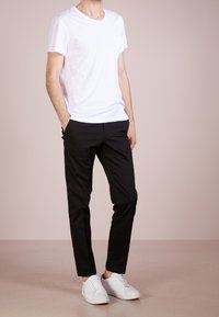 Biała koszulka z krótkim rękawem i kieszenią, w połączeniu z czarnymi spodniami slim fit i białymi trampkami, na jasnoróżowym tle.