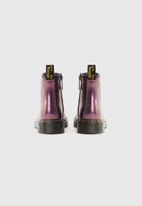 Botas de tobillo con cremallera metálica púrpura y superficie texturizada, suelas de goma negras y distintivas etiquetas de marca amarillas en la parte trasera.