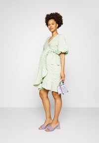 Vestido verde floral com mangas bufantes e bainha em renda, combinado com sandálias de salto bloco lilás e uma pequena bolsa lilás.