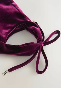 Bentita din catifea de culoare mov intens, cu un design rasucit si inchidere cu snur, avand accente metalice la capetele snururilor.