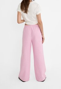 Pantalons larges rayés roses avec une taille élastique et un tissu doux, présentant des rayures blanches verticales pour plus de détail.