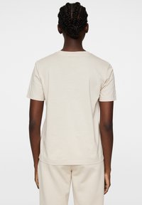 Beige bomullströja med rund halsringning, korta ärmar och en avslappnad passform; har en slät yta och inga synliga mönster eller dekorationer.