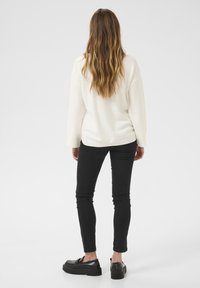 Vit, texturerad tröja med långa ärmar, kombinerad med svarta, åtsittande jeans och svarta platåskor. Outfiten ses från baksidan.