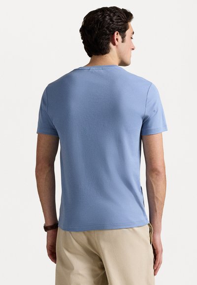 Heleheline puuvillane T-särk, nähtav seljast, lühikeste varrukatega ja klassikalise ümmarguse kaelusega, koos beežide pükstega.