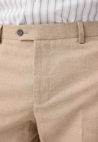Pantalones rectos en beige con un sutil tejido texturizado, con corte plano, pasadores para cinturón y un cierre de un solo botón.