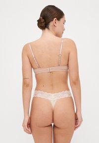 Blote lace-beslagde string en bh-set met verstelbare bandjes, zacht materiaal en golvende lace randen, getoond vanuit een achteraanzicht.
