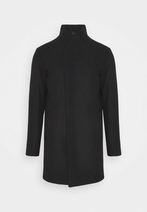 Zwarte wollen jas met een hoge kraag, met een eenvoudig ontwerp, lange mouwen en een rechte silhouet. Geen zichtbare sluitingen of accenten.