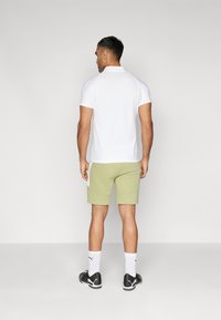 Camisola polo de manga curta branca, calções verdes claros, meias desportivas brancas com riscas pretas e ténis pretos. Acabamento de tecido suave.