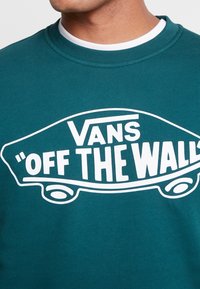 Sudadera de color verde azulado hecha de una mezcla de algodón con un acabado acanalado. Presenta un gran gráfico blanco de "Vans 'OFF THE WALL'" y un cuello redondo casual.