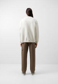 Sudadera blanca con un ajuste relajado y puños acanalados, combinada con pantalones cargo marrones que tienen un bolsillo lateral y un diseño de pierna ancha.