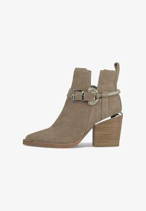 Beżowe zamszowe botki za kostkę z ostrym noskiem, srebrnym detalem w postaci klamry oraz wzorzystym drewnianym obcasem blokowym z metalicznym akcentem.