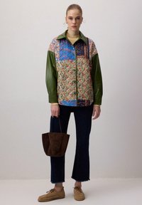 Multifarvet patchworkjakke med grønne læderærmer, blomsterprint og kravez. Båret med mørke jeans og en brun taske.