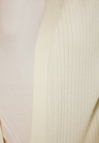 Cardigan crem cu dungi, cu o textură moale și un design cu fața deschisă, având un luciu subtil și margini stilate.