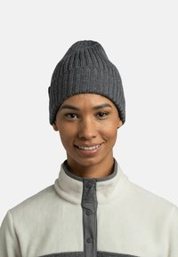 Gray knit beanie with vertical ribbing, pointed top, worn with a white fleece jacket featuring a gray zip and buttons.