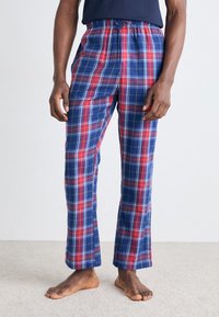 Pantalon de pyjama à carreaux bleus et rouges avec une taille élastique, jambes droites et une texture de tissu douce. Porté sans chaussures.