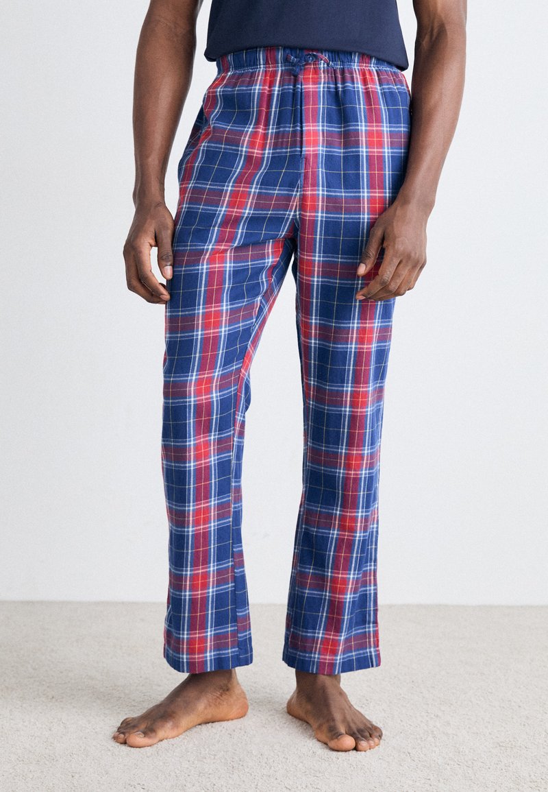 Pantalon de pyjama à carreaux bleus et rouges avec une taille élastique, jambes droites et une texture de tissu douce. Porté sans chaussures.