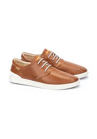 Zapatos de piel marrón con textura perforada, suela de goma blanca y cordones en contraste. Presentan acentos cosidos y detalle de marca en la lengüeta.