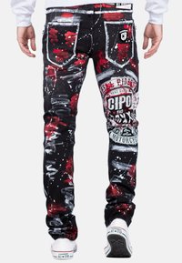 Jeans en denim noir avec éclaboussures de peinture rouges et blanches, dotés de poches arrière distinctes, de patchs de marque et d'une coupe slim.