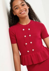 Rød ribbet strik top med korte ærmer, peplum kant, bølget frontpanel og pyntet med cirkulære falske perler.