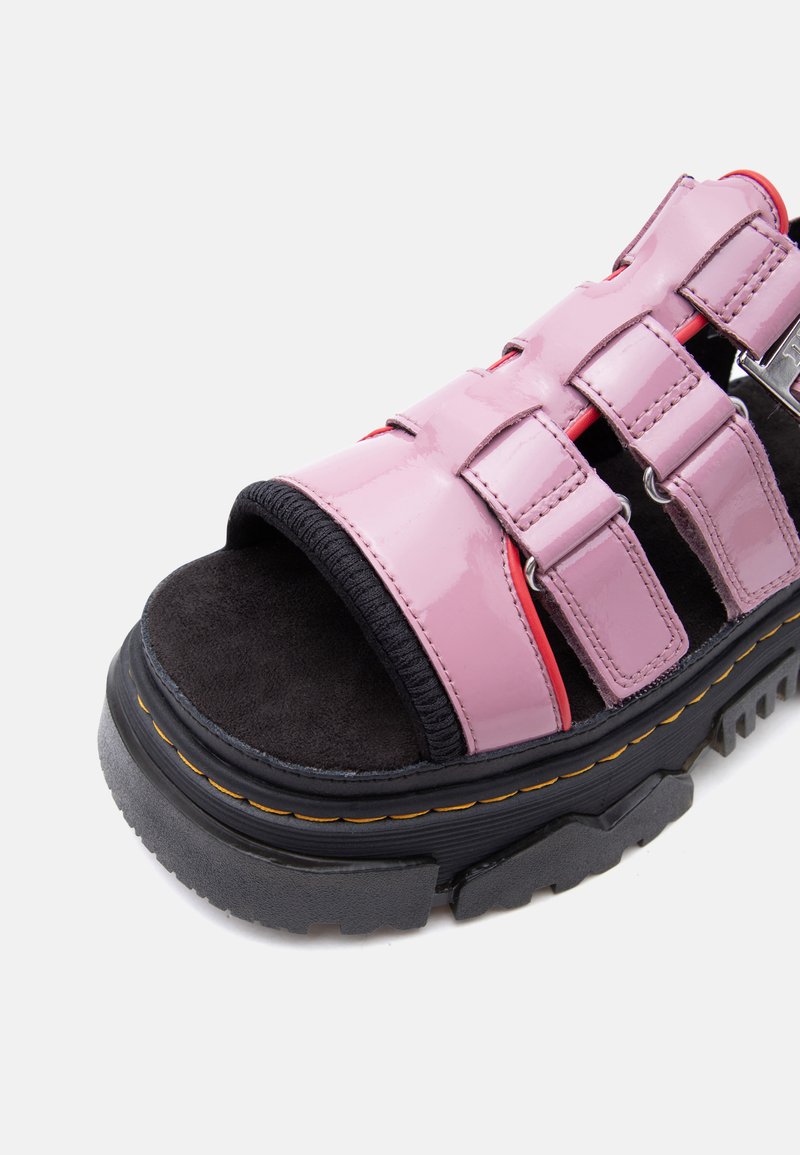 Sandalo con suola nera spessa, cinturini spessi in pelle verniciata rosa e punta aperta, fissato da tre fibbie regolabili.