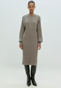 Strickkleid aus geripptem Material in Taupe mit rundem Halsausschnitt und langen, puffigen Ärmeln. Kombiniert mit eleganten, knielangen schwarzen Absatzstiefeln.